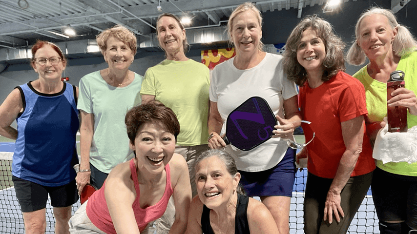 eight smiling older women on pickleball court