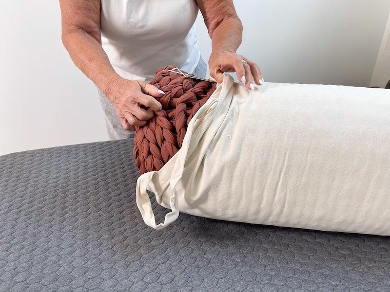 A woman pulls the Silk & Snow Hand Knitted Weighted Blanket out of its carrying case