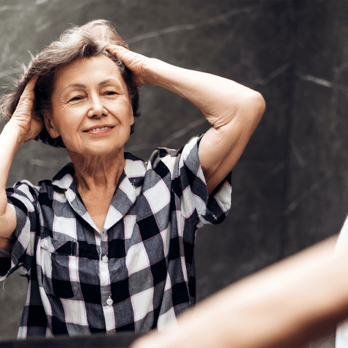A woman standing in front of a mirror with her hands in her hair