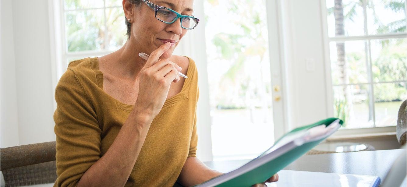 A senior woman is looking over a financial file, contemplating her decisions.