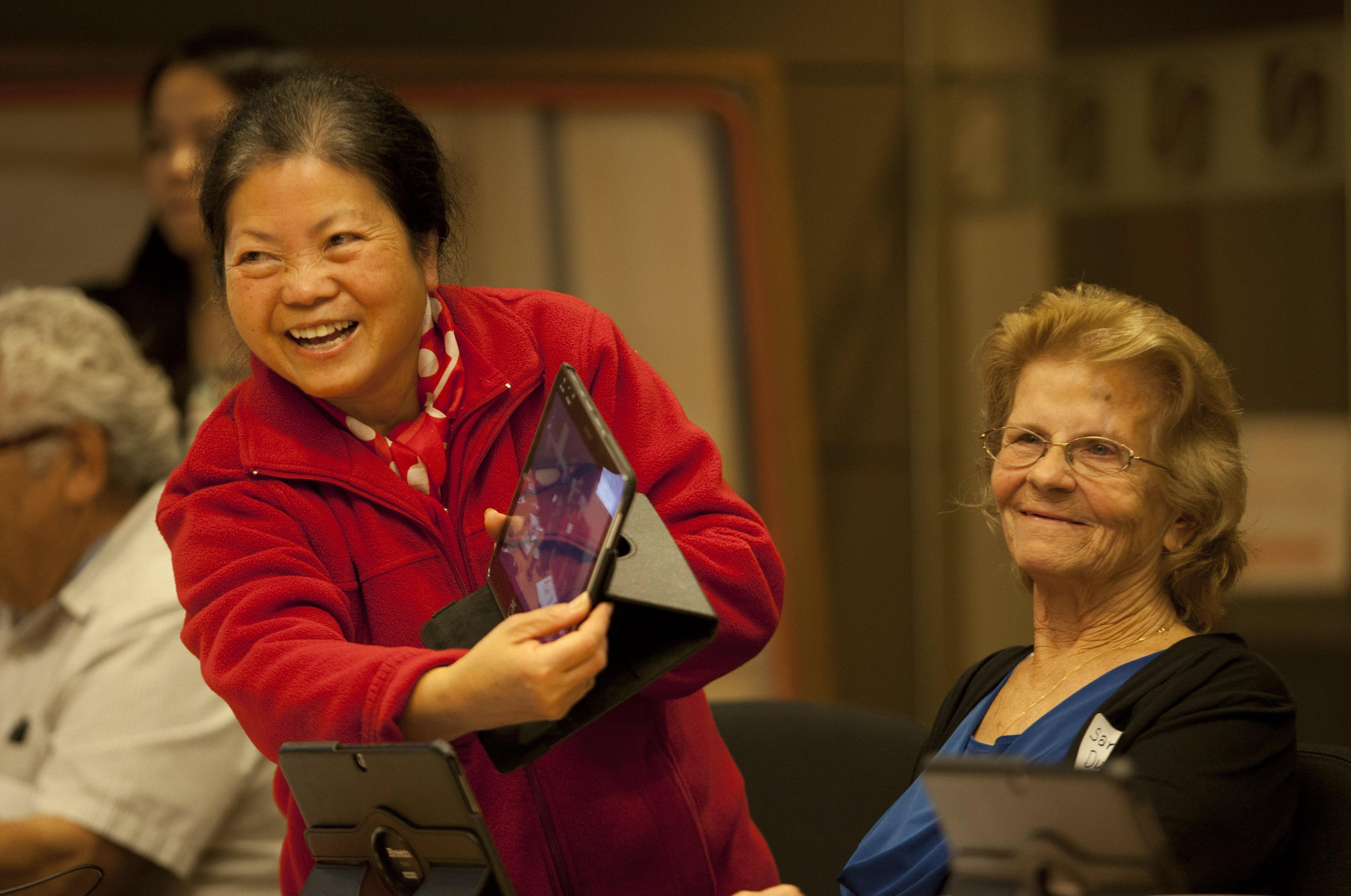 smiling older Asian woman showing a tablet to friends