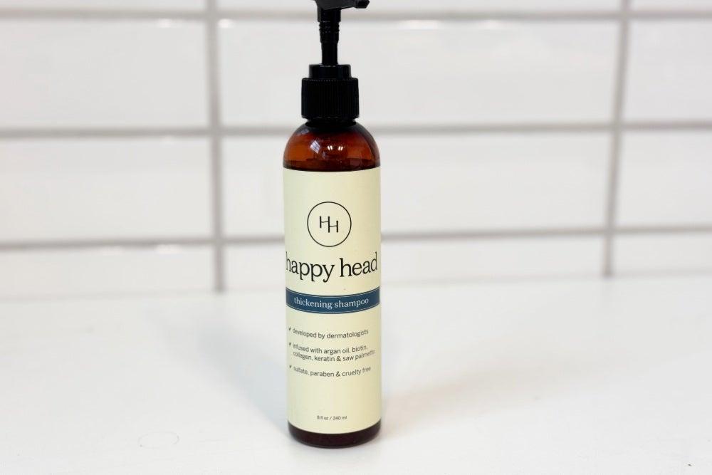 A bottle of Happy Head Thickening Shampoo on a white countertop