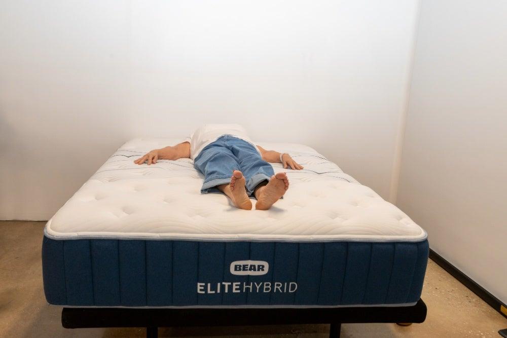 A woman lying on her back in the middle of the Bear Elite Hybrid mattress