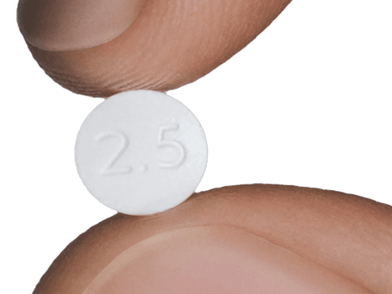 A tablet of Ro Oral Minoxidil held between a finger and a thumb