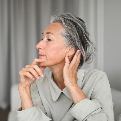 A woman with short silver hair looks at herself in a mirror