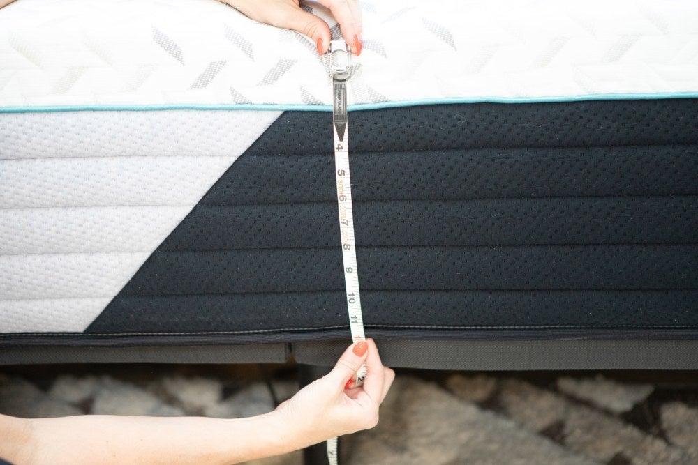 A woman measures the width of a mattress using a tape measure