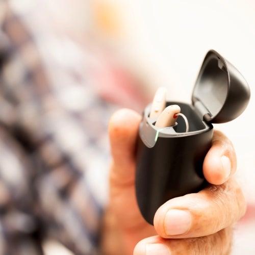 A close up image of a hand holding hearing aids in a portable case