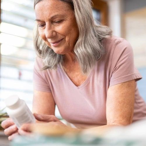 A woman with long grey hair inspects a supplement bottle