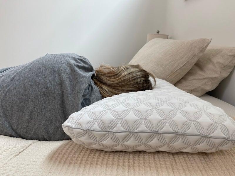A woman in a grey shirt lies on her side on the Brooklyn Bedding Talalay Latex Pillow with her back to the camera