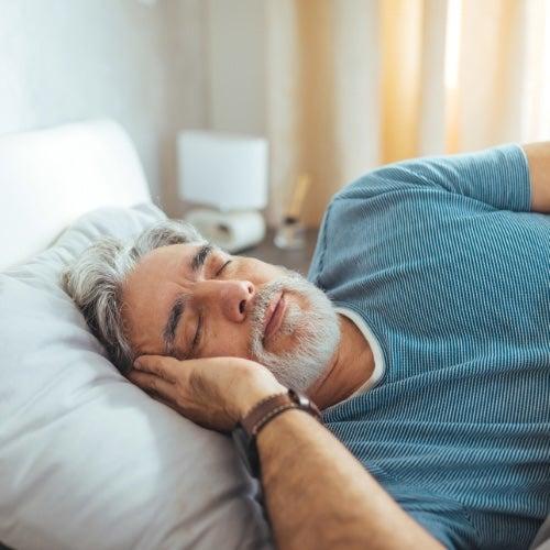 A man with grey hair relaxes on his side on a mattress