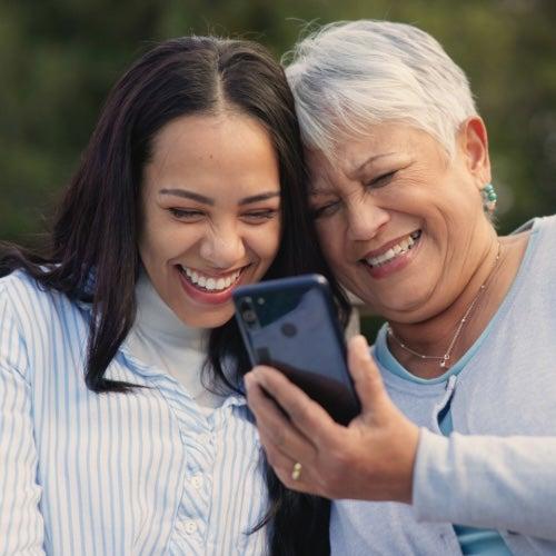 An older woman and younger woman look at a cellphone together and laugh