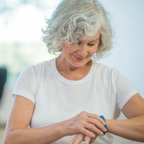 A smiling woman with grey hair checks the medical alert system on her wrist