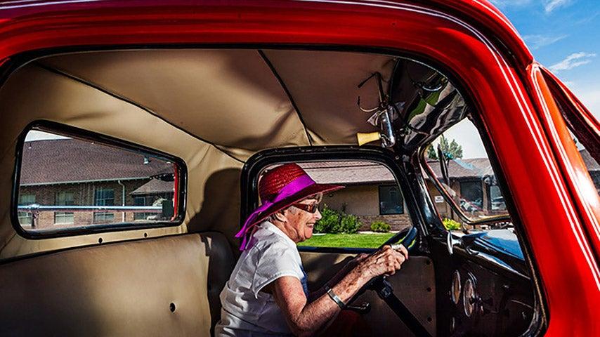 A woman smiles while driving an old red truck.