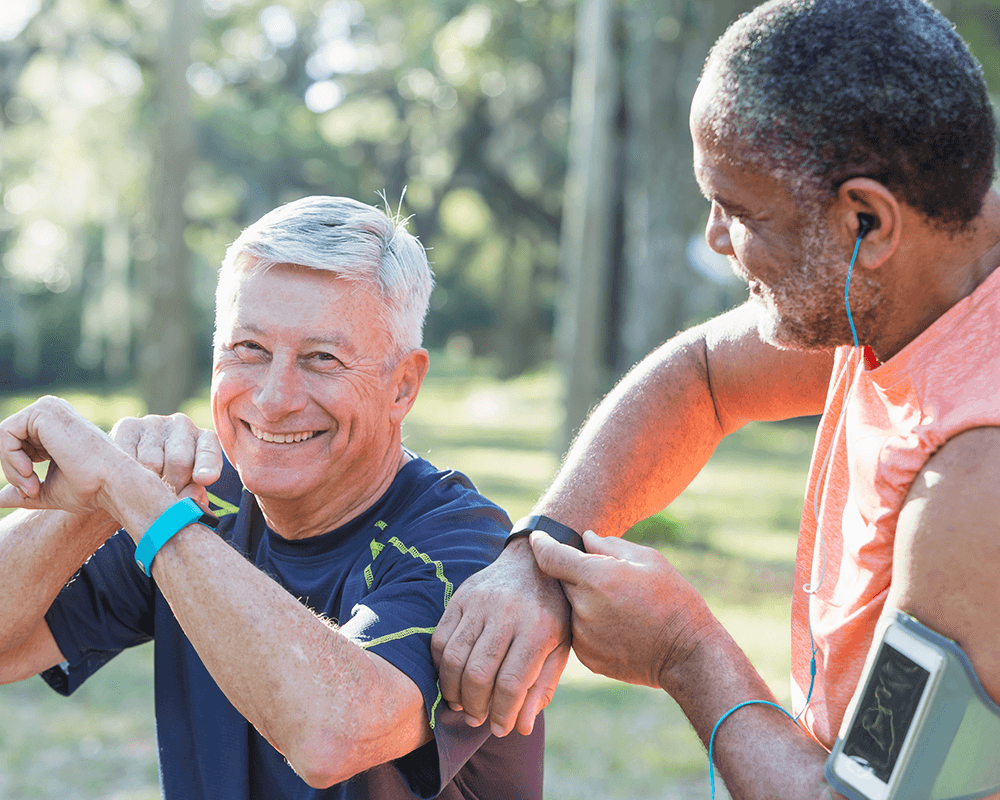 two older men smiling at each other as they touch their wrist fitness trackers