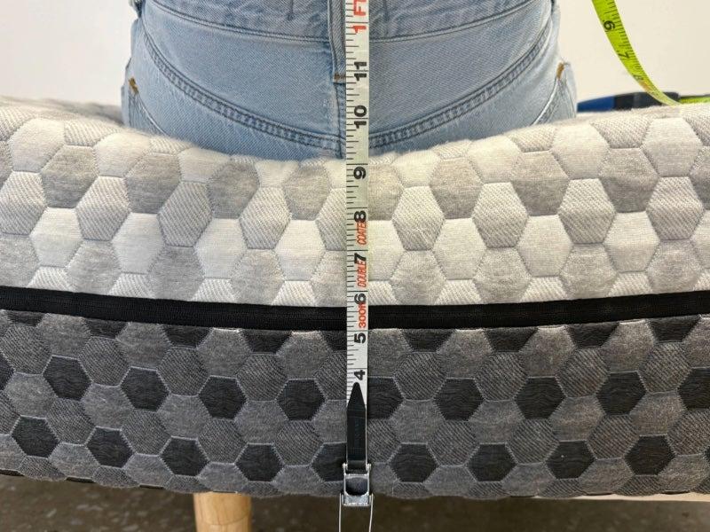 A person sitting backward at the edge of the Layla Memory Foam mattress and a measuring tape showing 9 inches