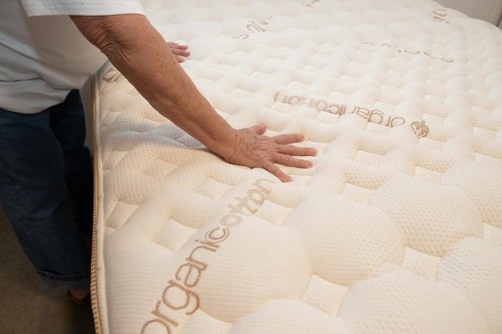 An older adult tester pushes down on the top of the Saatva Rx mattress