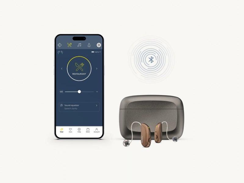 The Jabra Enhance Select M3 hearing aids, their case, and a smartphone with the Jabra app on the screen