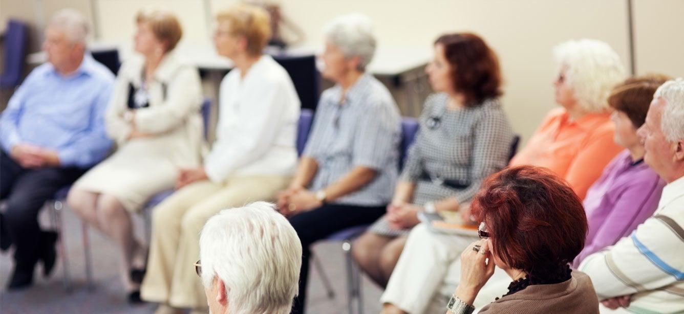 A group of seniors sits in a circle, listening during a training session.