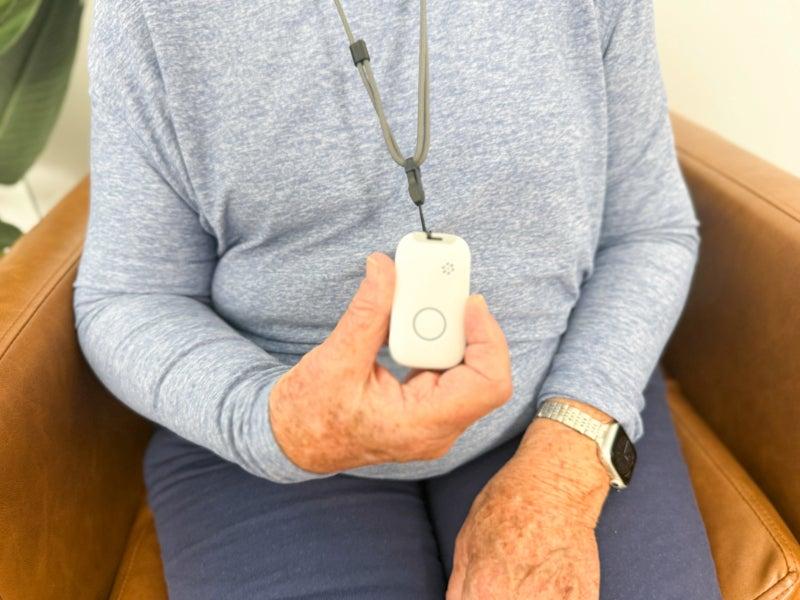 The white MobileHelp Elite, as worn against the torso of an older adult woman in a heather blue long-sleeve shirt