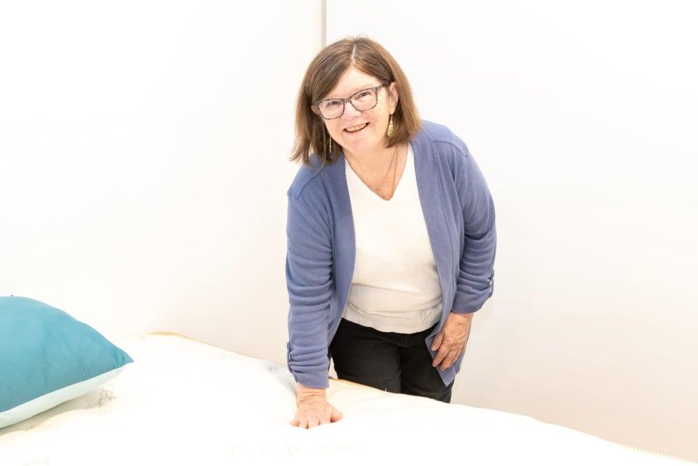 Woman pushes her hand down on the top of a mattress while smiling