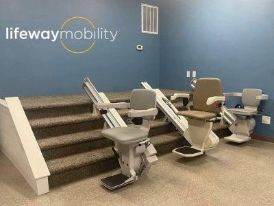 Three different stair lifts at the bottom of a small set of stairs in a Lifeway Mobility showroom