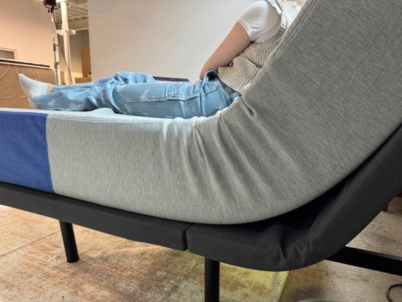 A person in jeans and a tan sweater rests in the Nectar adjustable base
