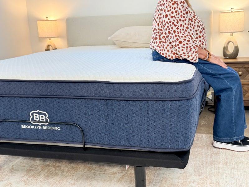 A person sitting on the edge of the Brooklyn Bedding Aurora Luxe mattress