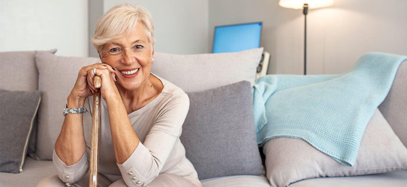 Smiling woman with short blonde hair and a cane on a light gray sofa