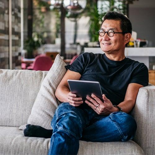 Man smiles while sitting on couch and holding tablet