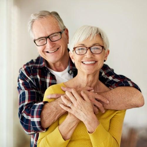 A man and a woman wearing glasses, smiling and hugging