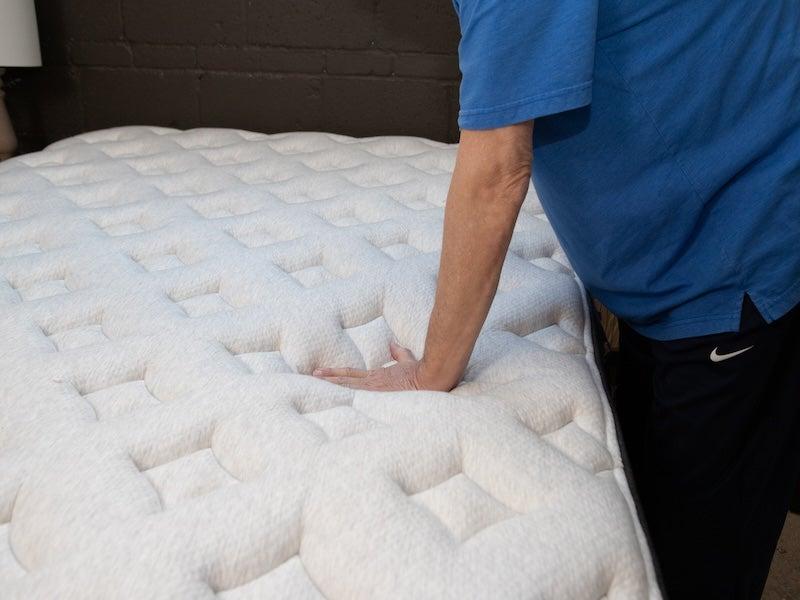 A man pushed down on the quilted mattress top of the Helix Midnight Luxe mattress