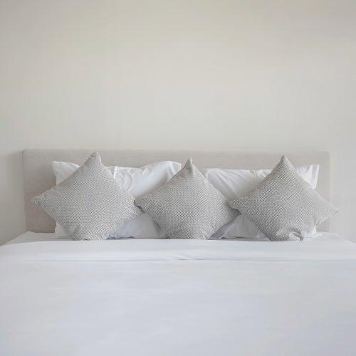 A white bed with grey pillows in a clean white room