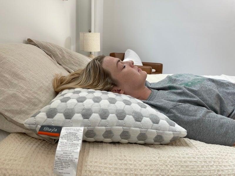A woman lies down with her head resting on the Layla Kapok pillow.