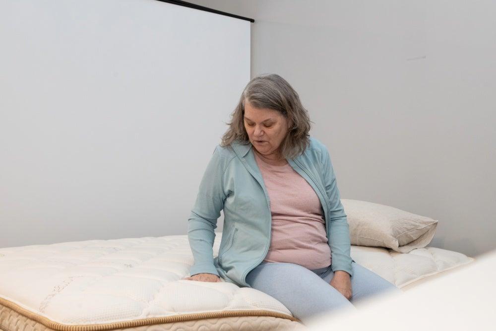 A woman sitting on the edge of the Saatva Solaire mattress