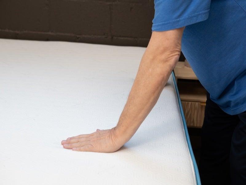 A man in a short-sleeved blue shirt presses on the topper of the Bear Original mattress