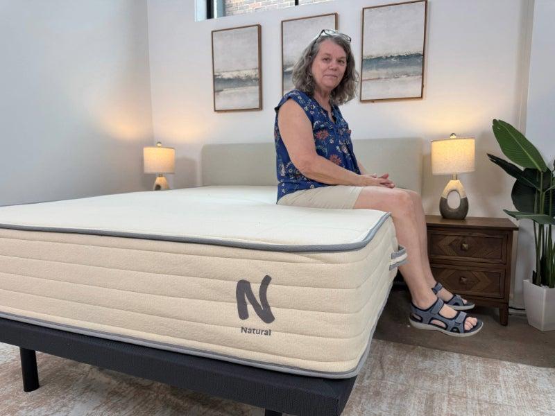 A woman sits on the edge of the Nolah Natural mattress.