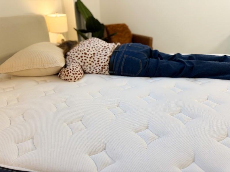 A woman in a red and white polka-dot shirt and jeans lies on her stomach on the Silk & Snow mattress.