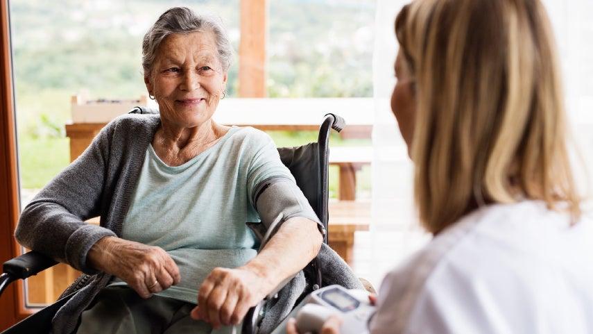 A senior woman in a wheel chair is smiling while getting her blood pressure taken.
