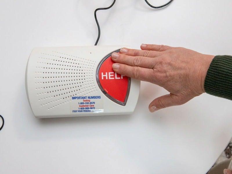 A man pressing a large help button on a medical alert system