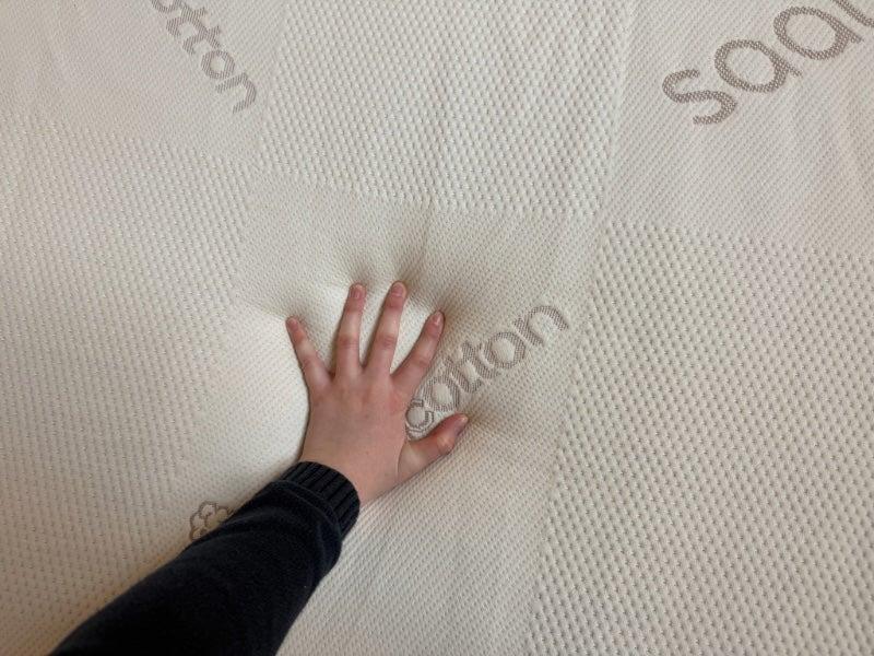 A hand pressing down on the top of the Saatva Natural Latex Mattress Topper