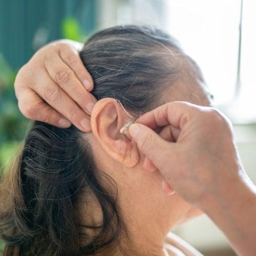 A woman placing a hearing aid into her ear