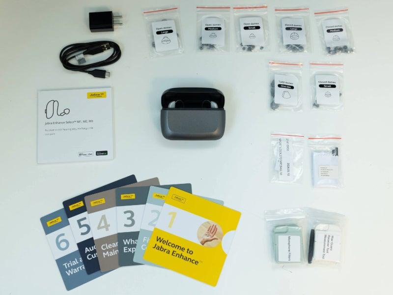 The Jabra Enhance Select M3 hearing aids, their case, user guide, instruction booklet, and other accessories