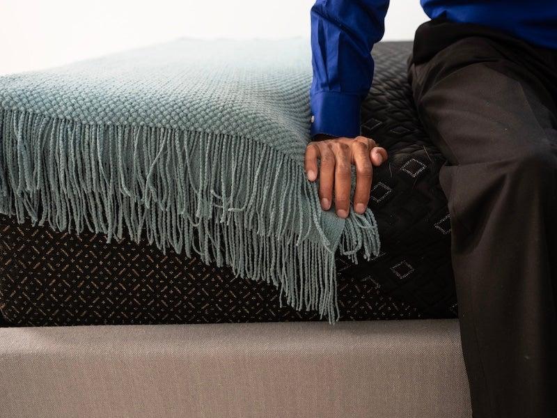 A man sits on the edge of the Beautyrest Black Hybrid XCS mattress