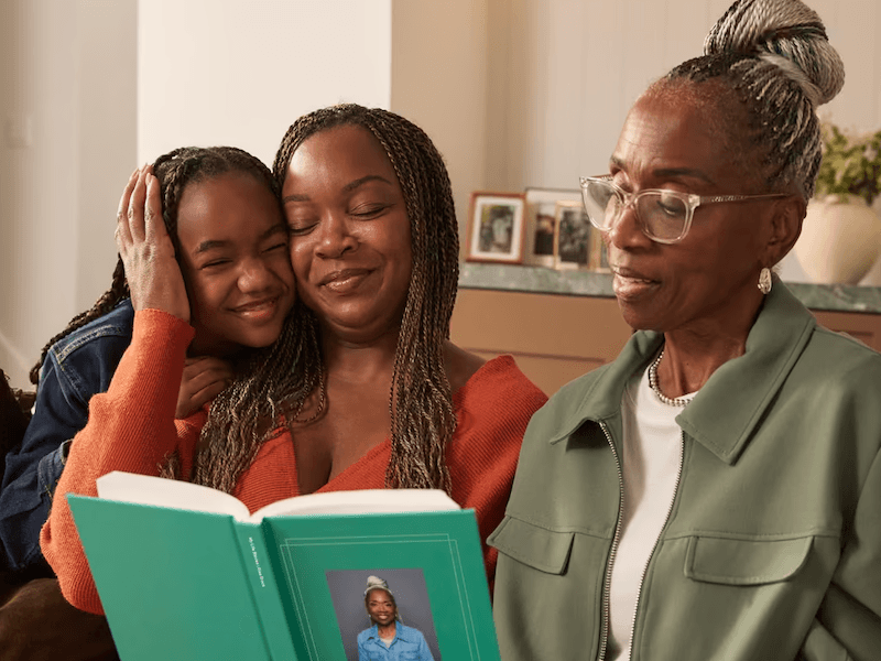 Three generations of women sit on a couch reading from a book together