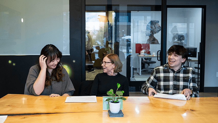smiling older woman with smiling younger man and woman at conference room table