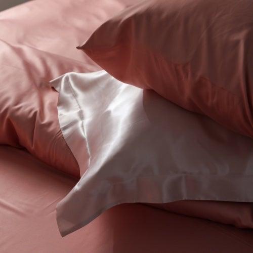 A pile of silk pillowcases in pink and white on a bed with silk sheets