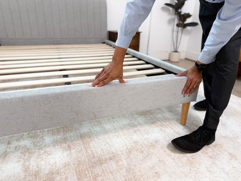 A man presses down on the end of the DreamCloud Claremont bed frame
