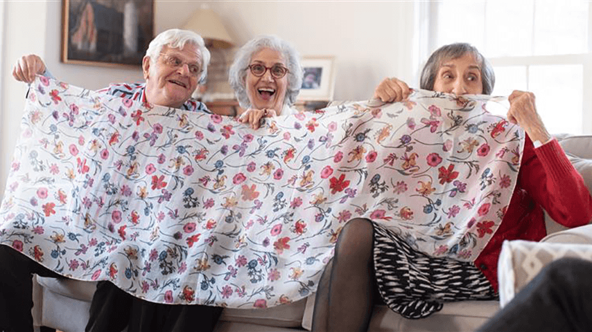 Three older adults sit together with a scarf