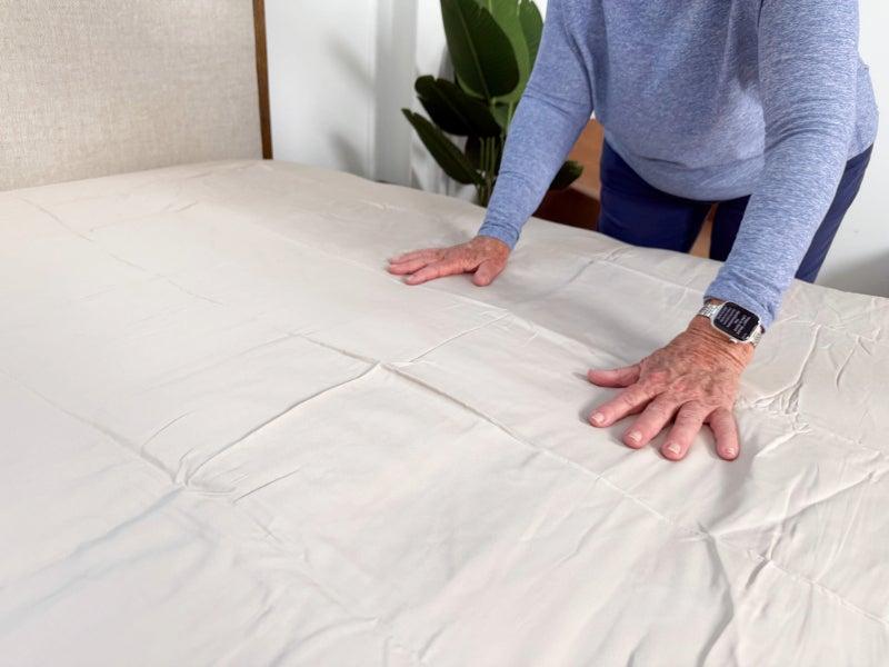 An older adult woman smoothing out the Quince Bamboo Sheet Set on a bed