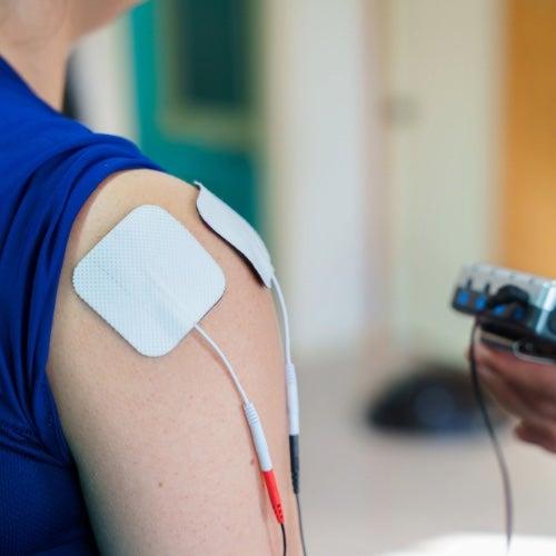 A health care provider operates a TENS unit attached to a person's arm with electrode pads